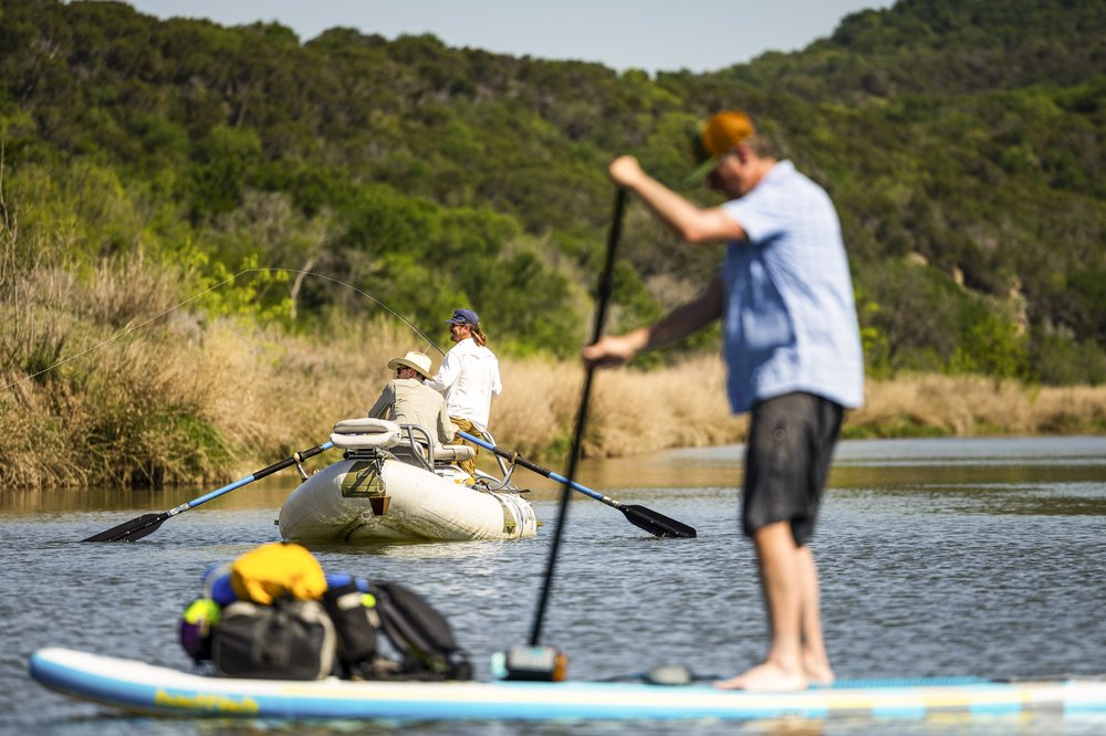 Male paddle boarder passing by two fishermen in small boat on Brazos River