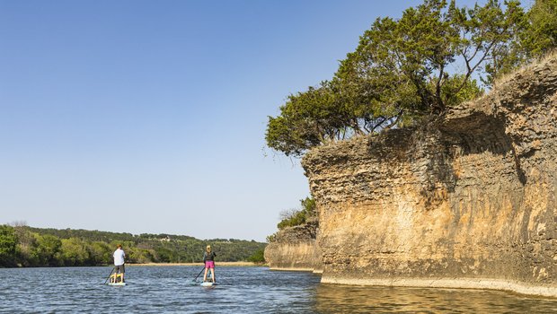 Pair of paddleboarders along a small cliff on the Brazos River