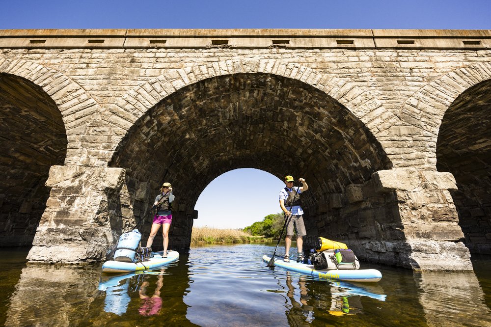 Pair of paddleboarders paddling through the arches of Possum Kingdom Stone Arch Bridge on the Brazos River