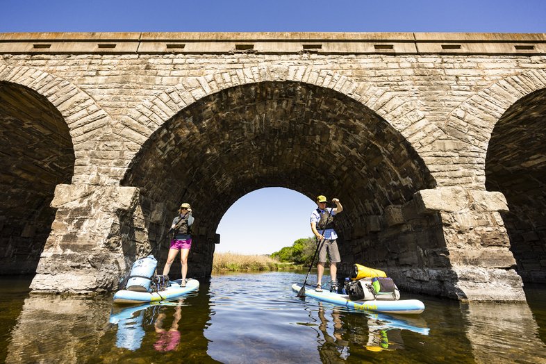 Pair of paddleboarders paddling through the arches of Possum Kingdom Stone Arch Bridge on the Brazos River