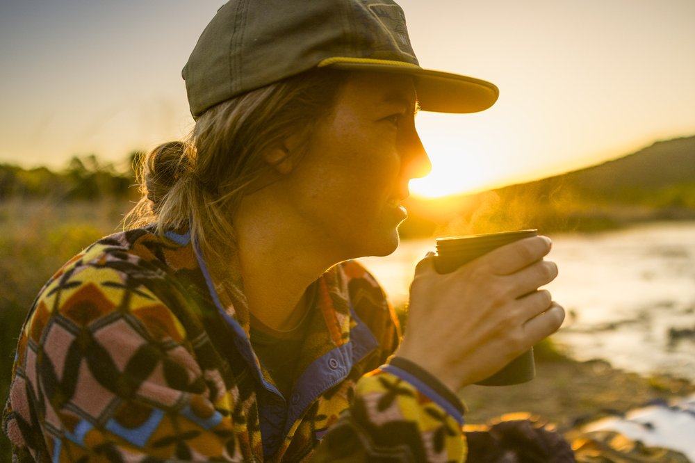 Female camper enjoying a hot coffee at sunrise on the Brazos Riverbank