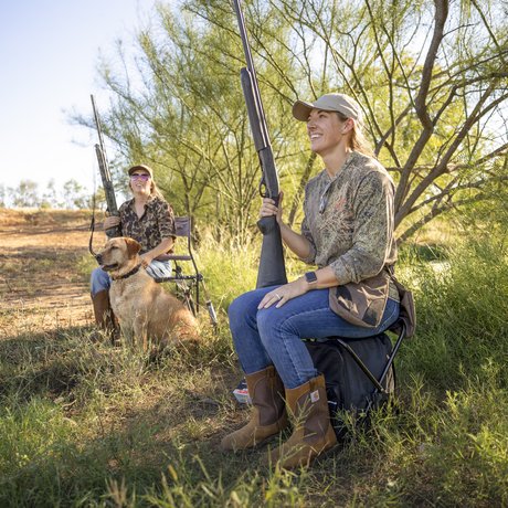 Two women in field in south Texas hunting dove with shotguns and a dog