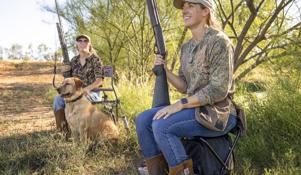 Two women in field in south Texas hunting dove with shotguns and a dog