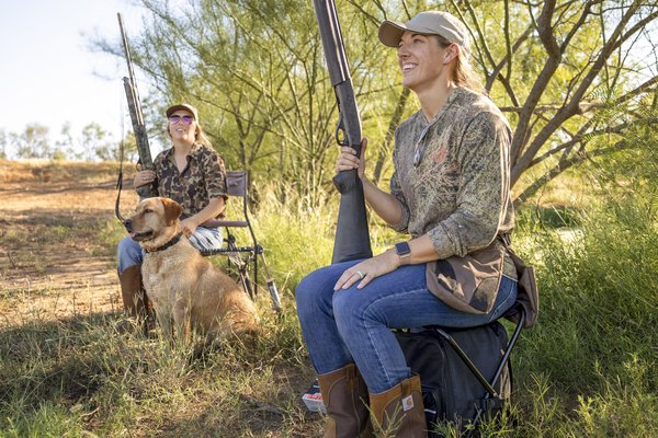 Two women in field in south Texas hunting dove with shotguns and a dog