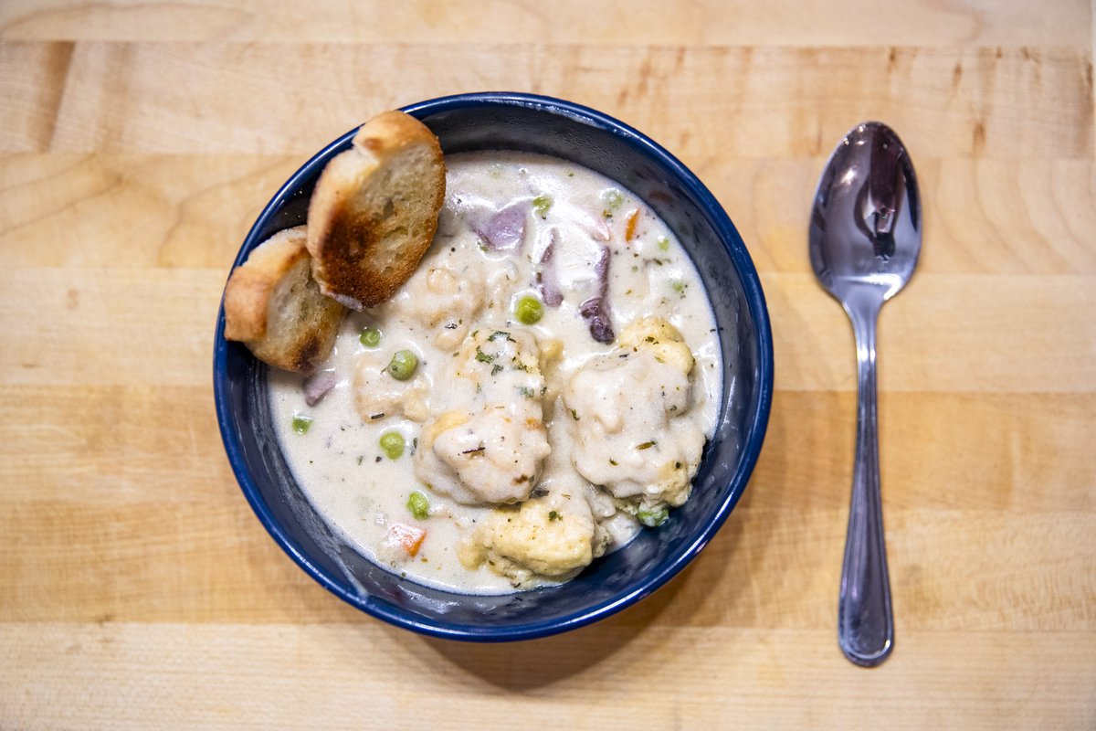 Dove and dumpling soup with two pieces of bread in a blue bowl with spoon
