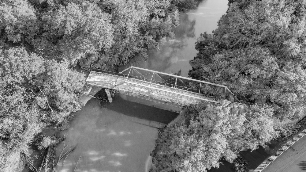 A black and white photo of a bridge over a creek.