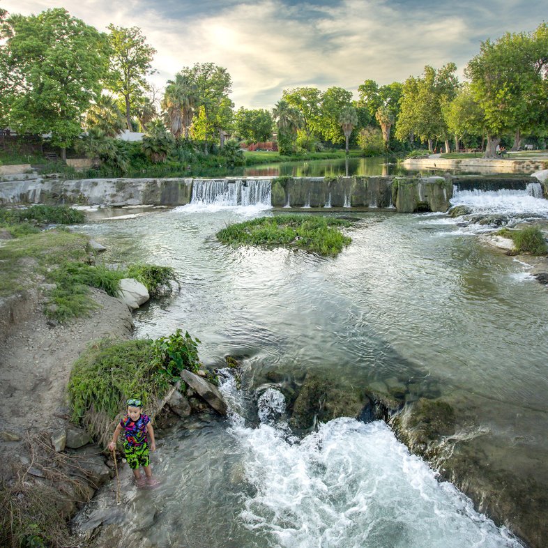 A person in a creek standing in a pool of shallow rapids.