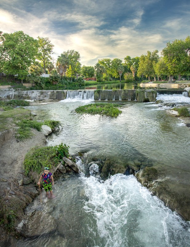 A person in a creek standing in a pool of shallow rapids.