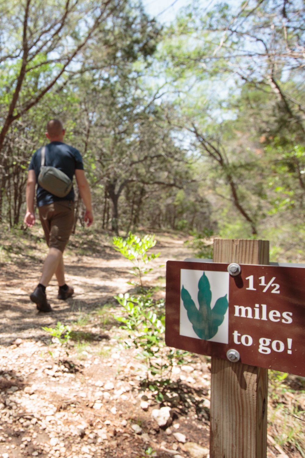 Man hikes by sign showing 1.5 miles to go to dinosaur tracks