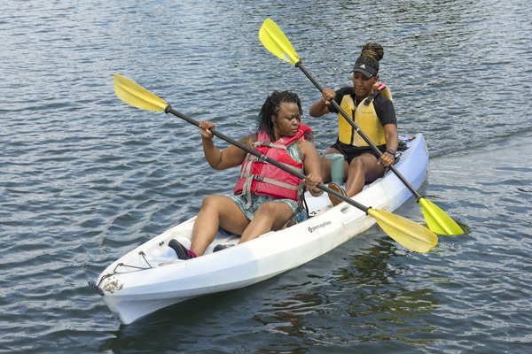 Two women paddle a tandem kayak