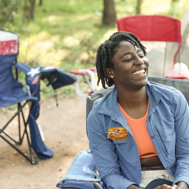An African American woman smiles while sitting on a camp chair in front of a tent