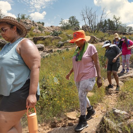 A set of African American women hiking a trail single file, shown in profile