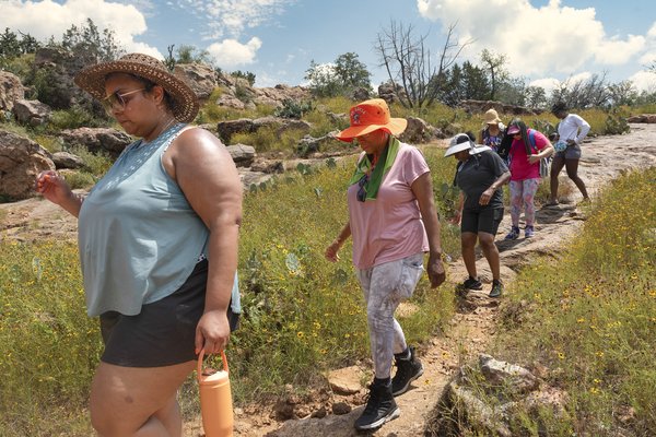 A set of African American women hiking a trail single file, shown in profile