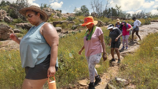 A set of African American women hiking a trail single file, shown in profile