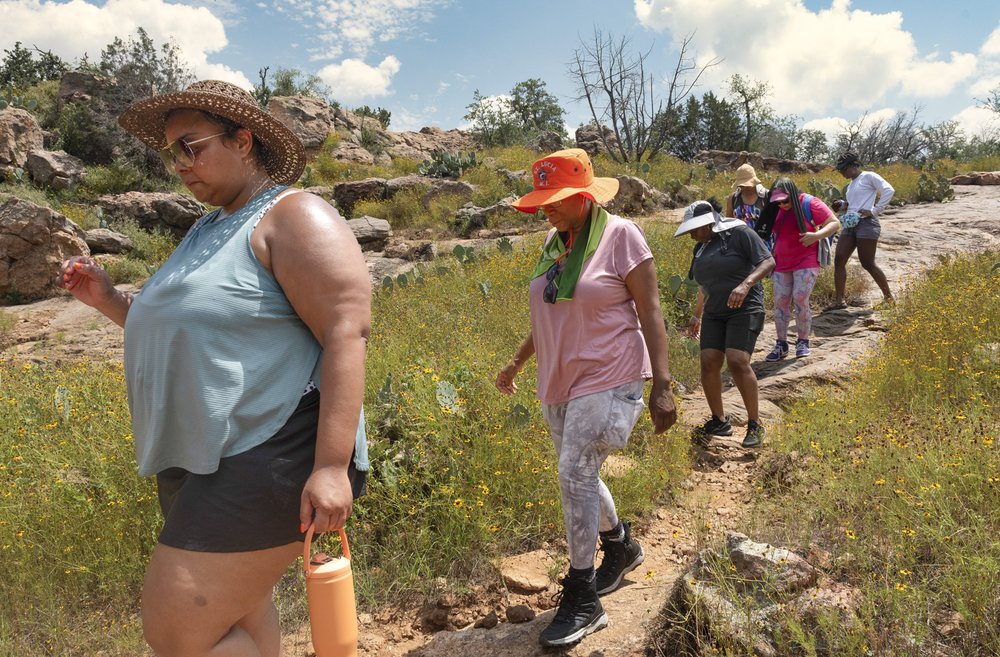 A set of African American women hiking a trail single file, shown in profile