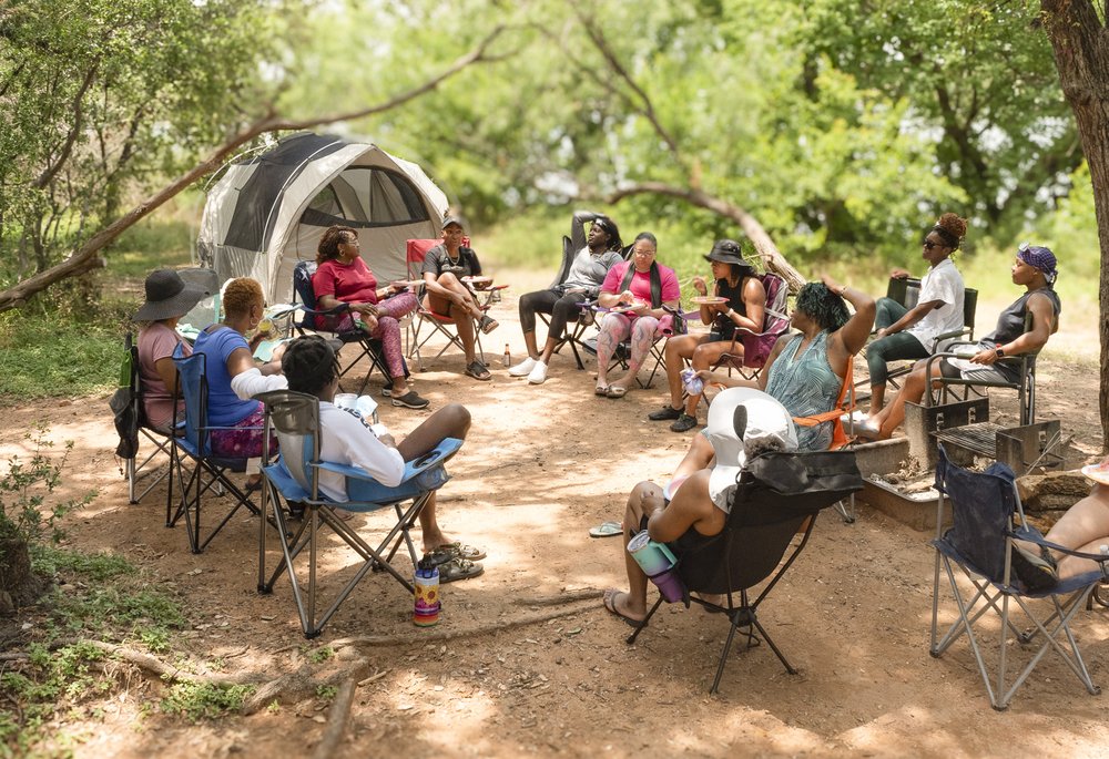 A group of African American women gather around a camp site in the late afternoon