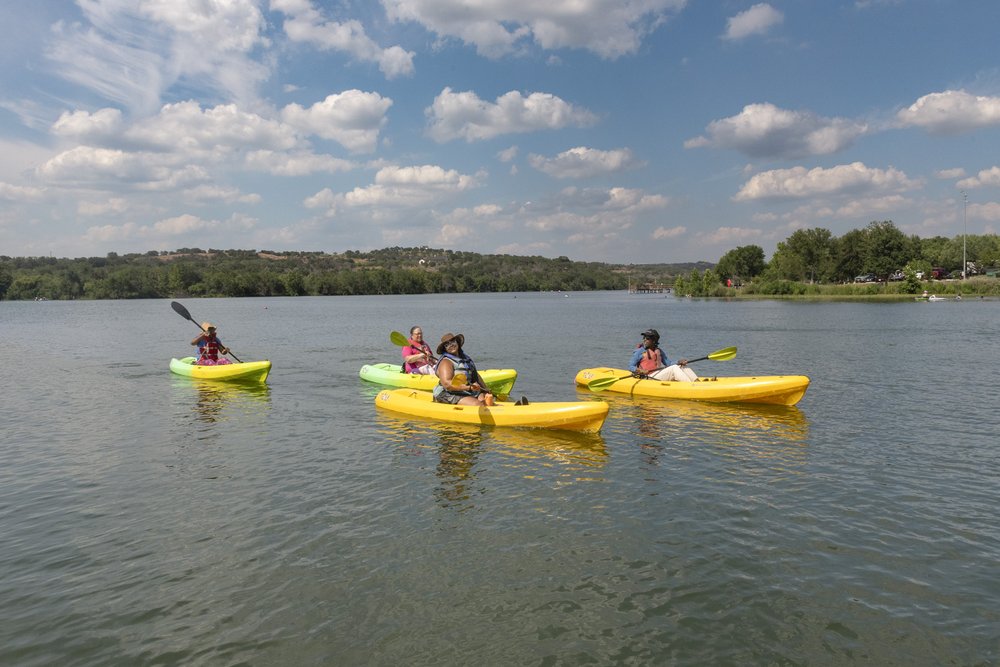 Four African American women paddle yellow kayaks across Inks Lake