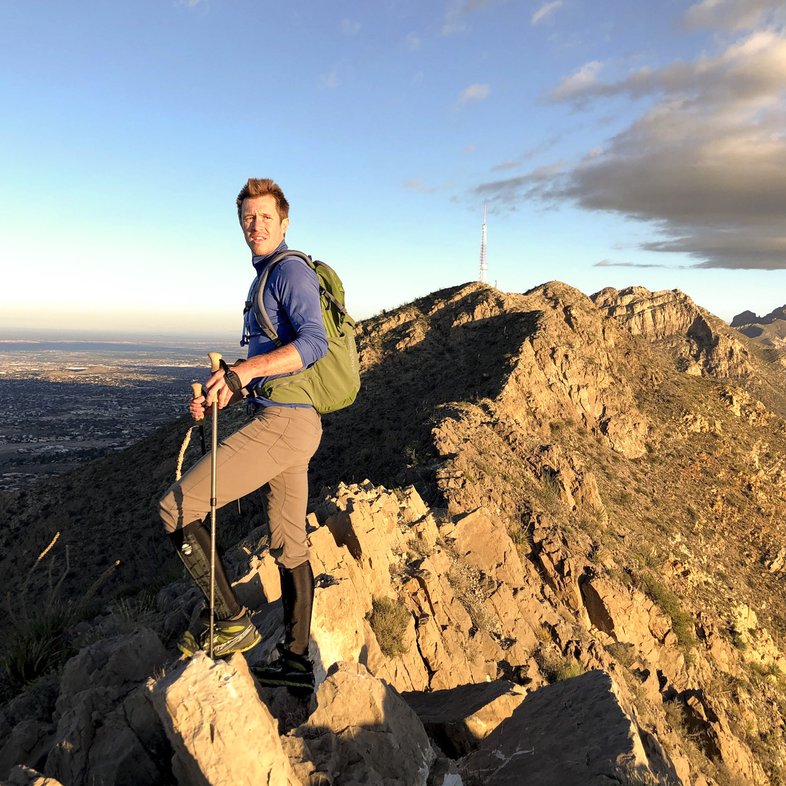 A male hiker holding trekking poles stands along the ridgeline atop the Franklin Mountains