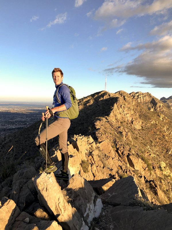 A male hiker holding trekking poles stands along the ridgeline atop the Franklin Mountains