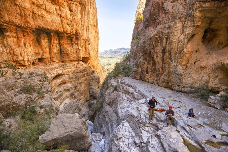 Two hikers stand in the rocky divide between two cliffs