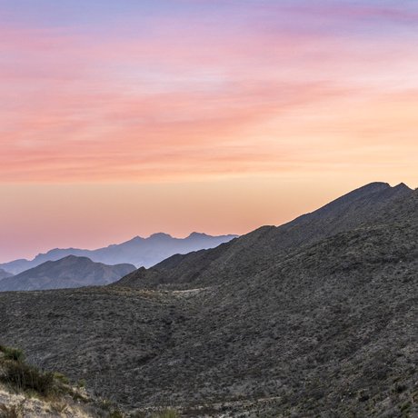 A pink and blue sky highlights the scrub-covered hills of the Franklin Mountains