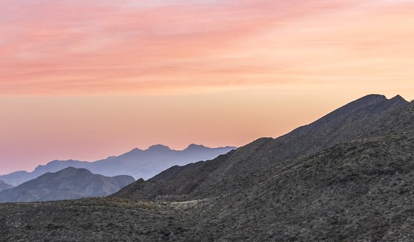 A pink and blue sky highlights the scrub-covered hills of the Franklin Mountains