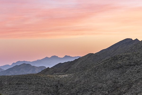 A pink and blue sky highlights the scrub-covered hills of the Franklin Mountains