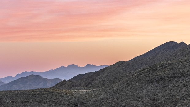 A pink and blue sky highlights the scrub-covered hills of the Franklin Mountains