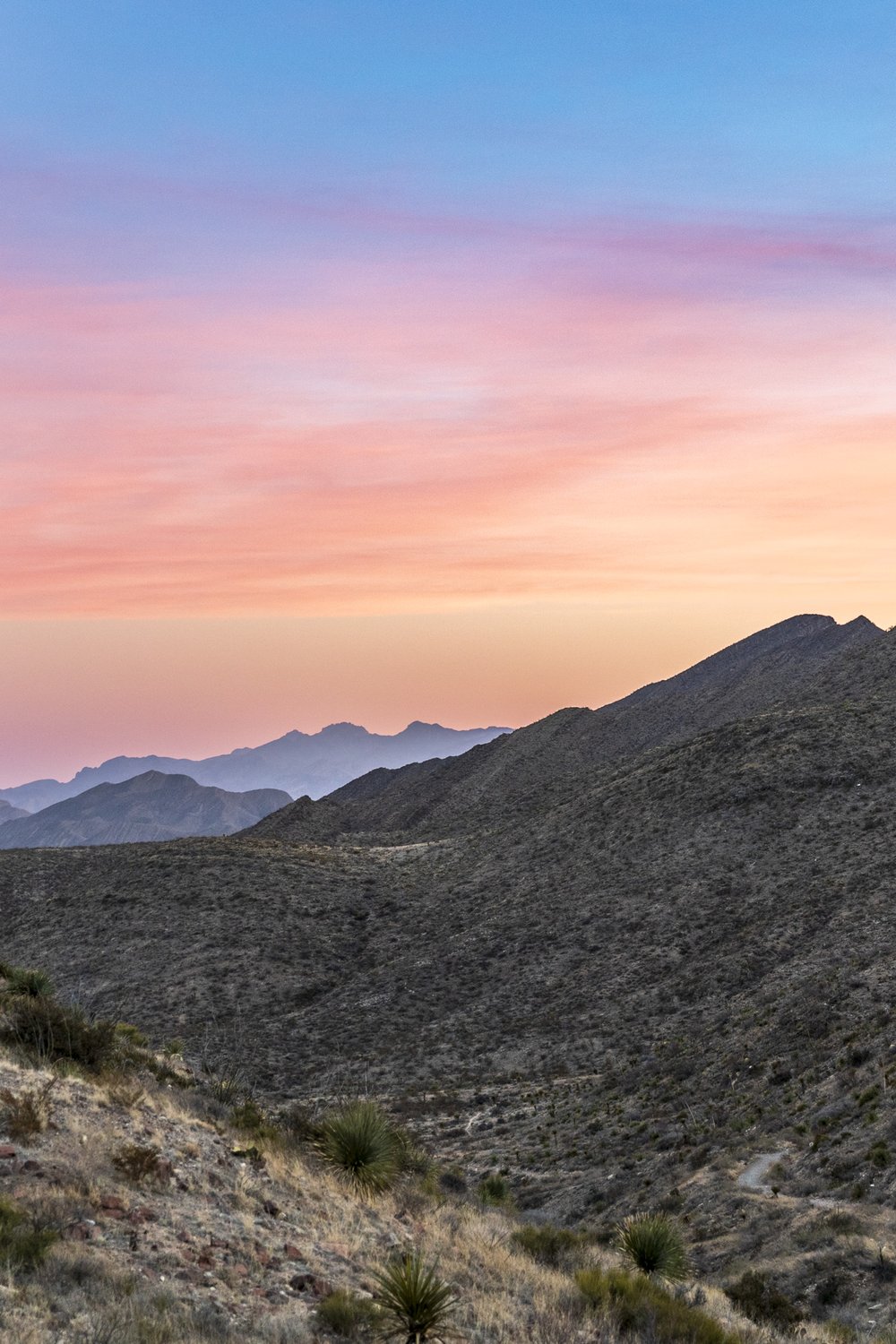 A pink and blue sky highlights the scrub-covered hills of the Franklin Mountains
