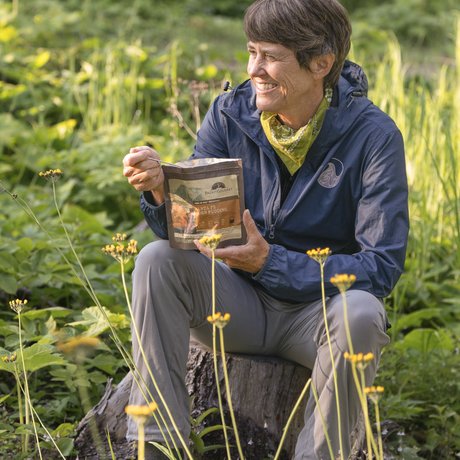 Writer Pam Leblanc sits on a rock and eats from a freeze-dried meal pouch