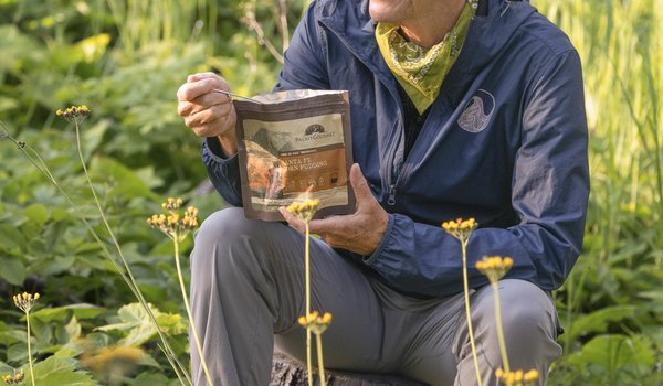 Writer Pam Leblanc sits on a rock and eats from a freeze-dried meal pouch