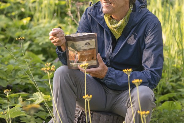 Writer Pam Leblanc sits on a rock and eats from a freeze-dried meal pouch