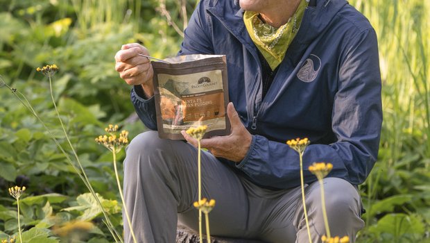 Writer Pam Leblanc sits on a rock and eats from a freeze-dried meal pouch