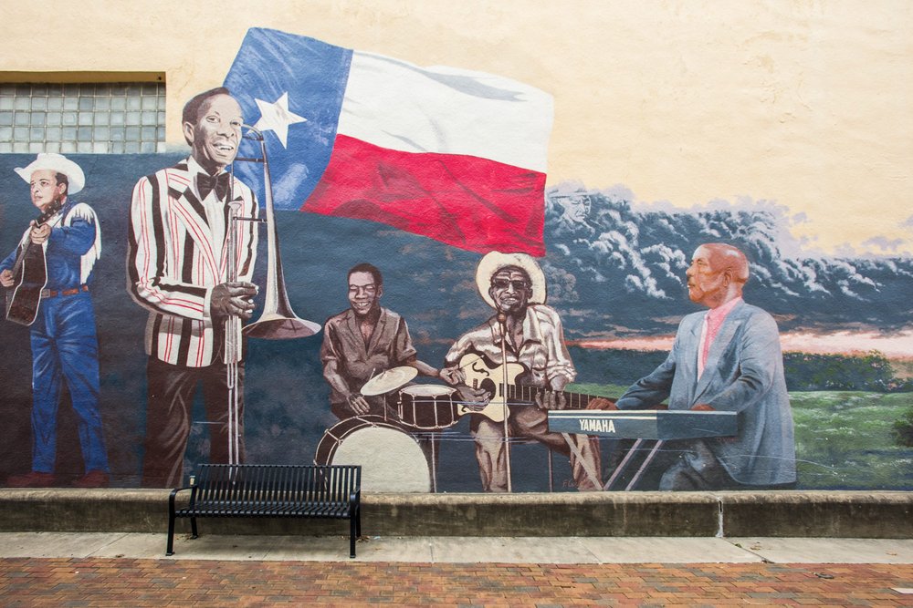 A mural of jazz musicians, including a trombone player, a drummer, a guitarist and a keyboard player playing in front of the Texas flag adorns a wall in Navasota Texas