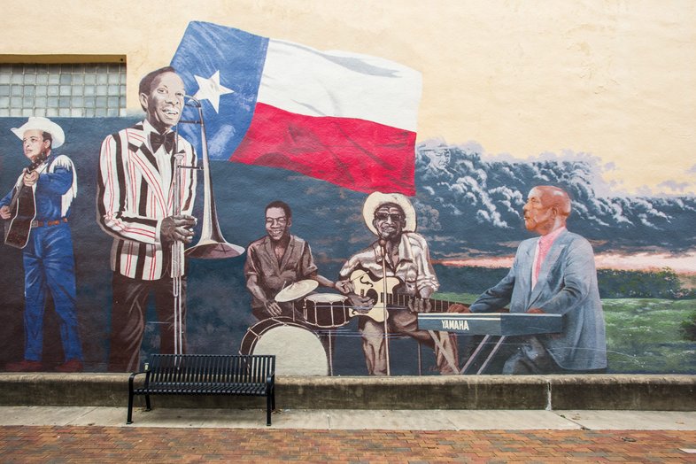 A mural of jazz musicians, including a trombone player, a drummer, a guitarist and a keyboard player playing in front of the Texas flag adorns a wall in Navasota Texas