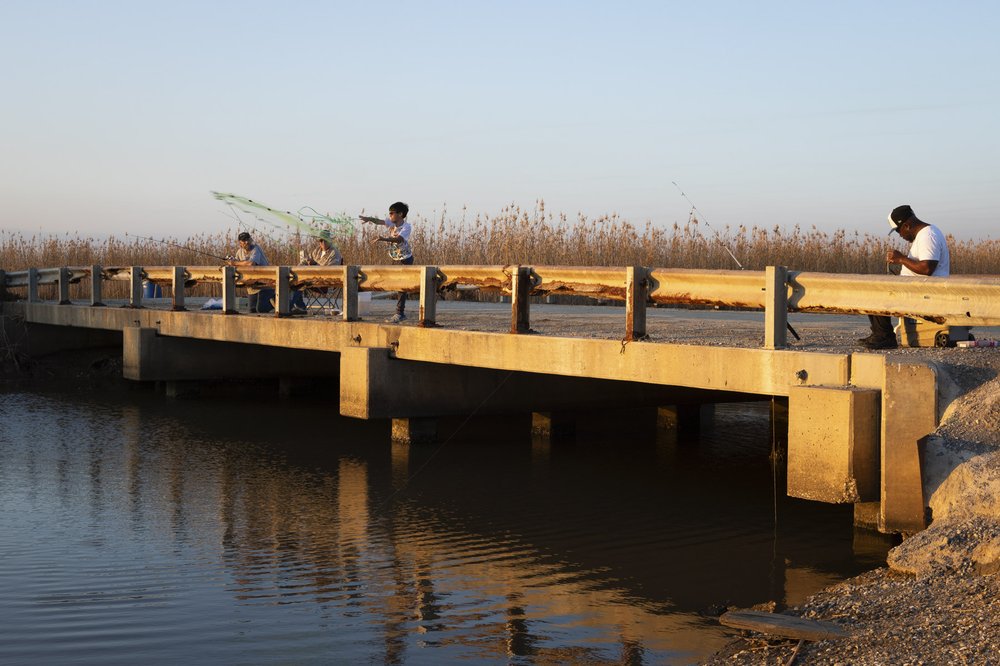 A father and grandfather watch as young boy cast a net of bridge over river at Lower Neches Wildlife Management Area.