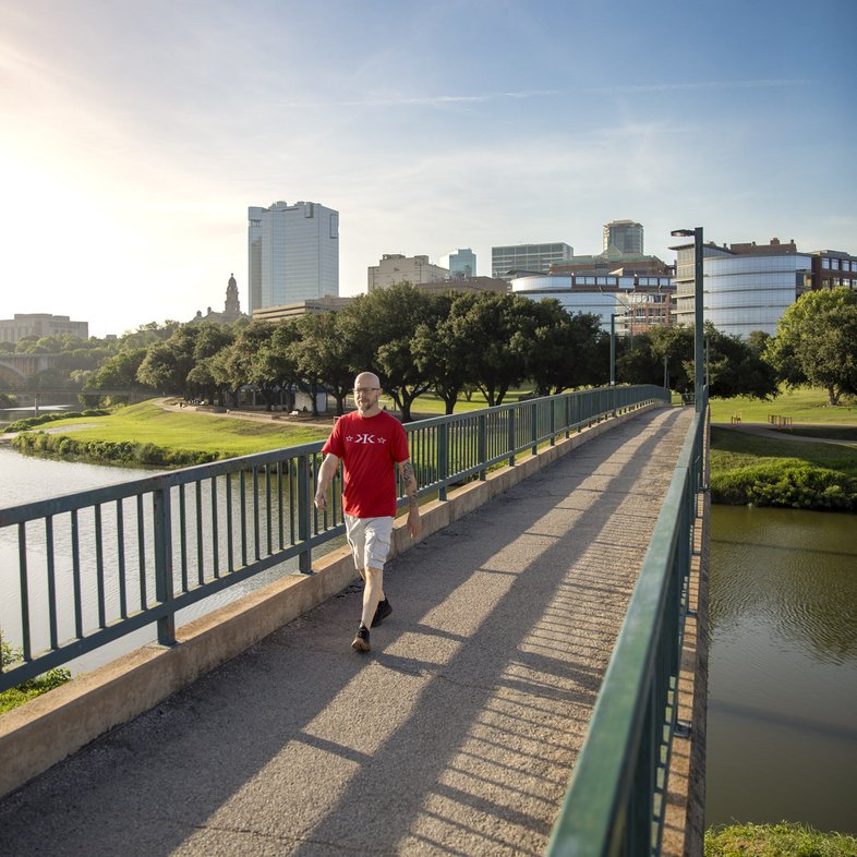 Man hiking on paved bridge over Trinity River with Fort Worth skyline in background