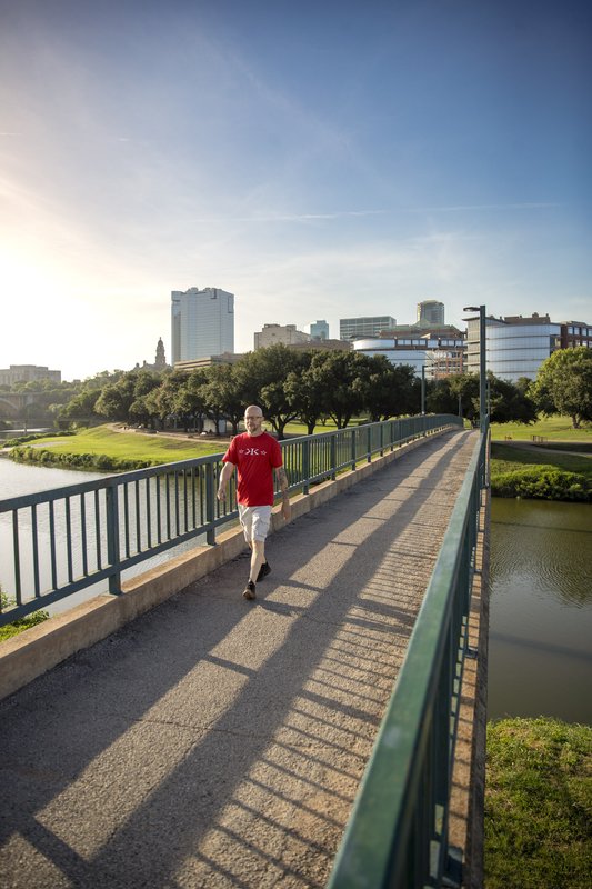 Man hiking on paved bridge over Trinity River with Fort Worth skyline in background