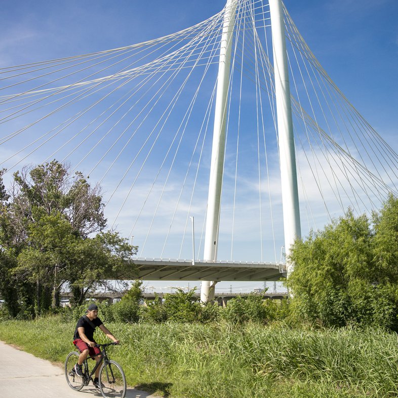 Man biking on paved The Loop trail with Margaret Hunt Hill cable-stayed bridge in background