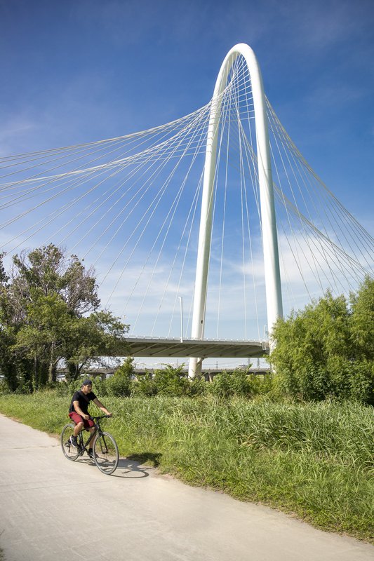 Man biking on paved The Loop trail with Margaret Hunt Hill cable-stayed bridge in background