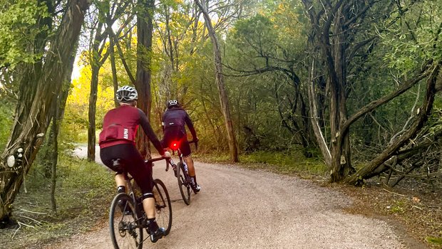 Two bikers on dirt trail surrounded by trees