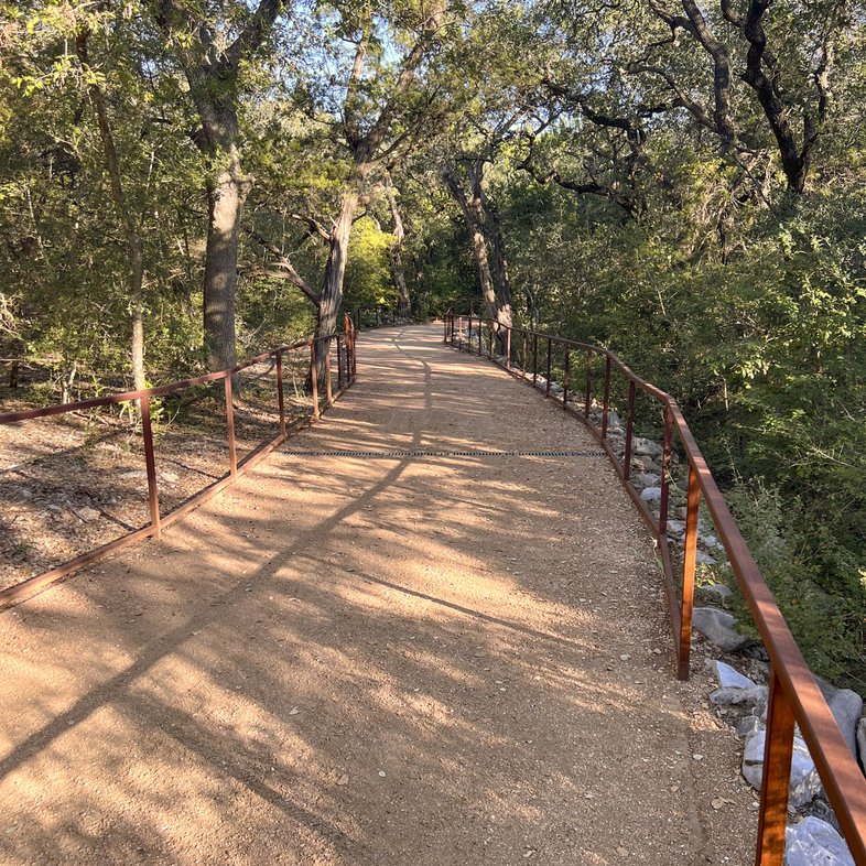 Dirt trail with railing over creek with trees