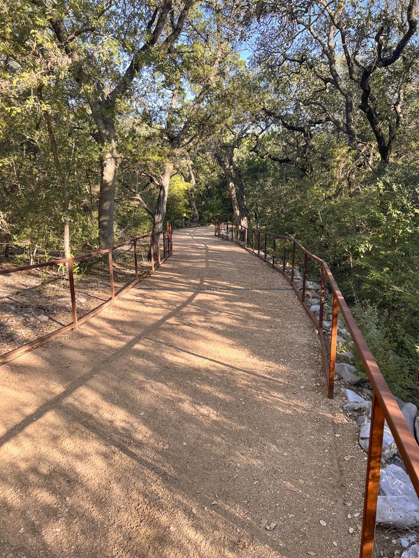 Dirt trail with railing over creek with trees