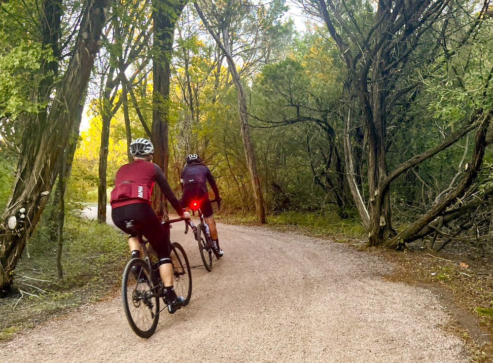 Two bikers on dirt trail surrounded by trees