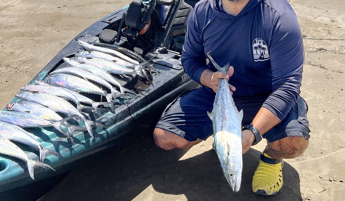 Fisherman holding Spanish mackerel next to fishing kayak on beach
