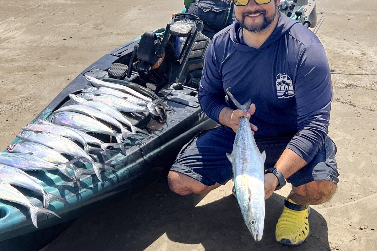 Fisherman holding Spanish mackerel next to fishing kayak on beach