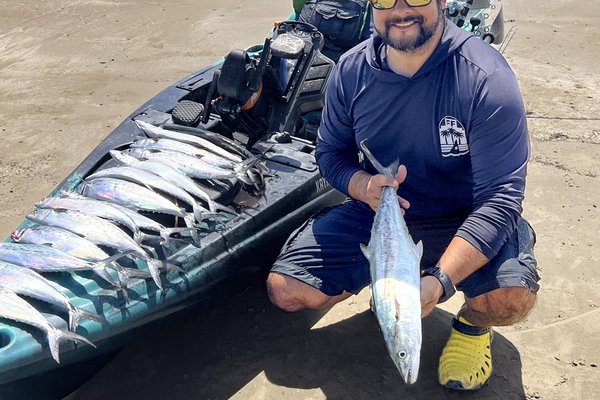 Fisherman holding Spanish mackerel next to fishing kayak on beach