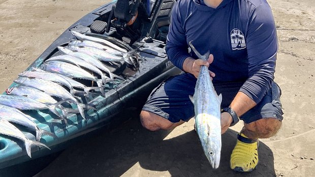 Fisherman holding Spanish mackerel next to fishing kayak on beach