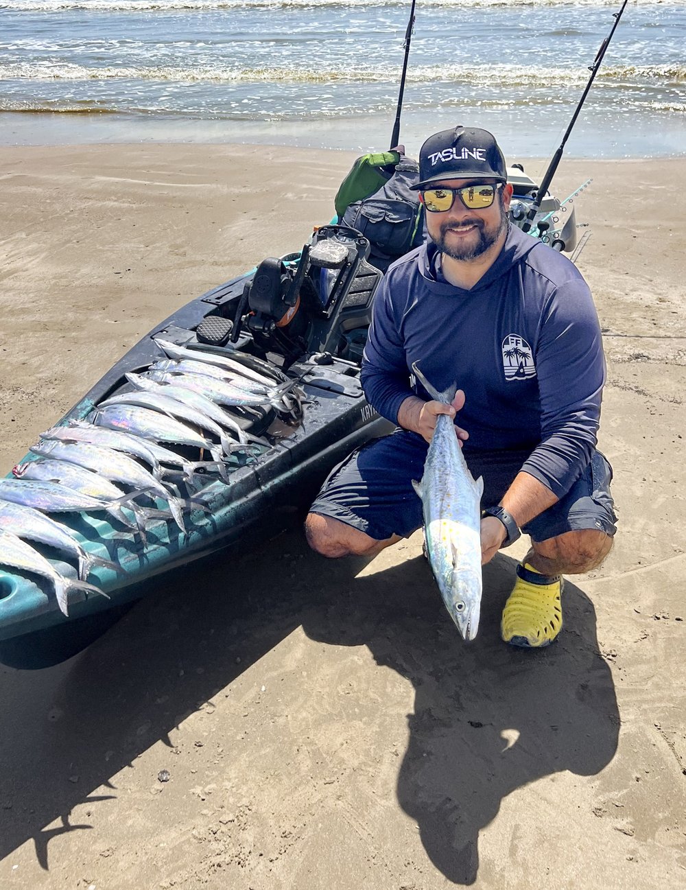 Fisherman holding Spanish mackerel next to fishing kayak on beach