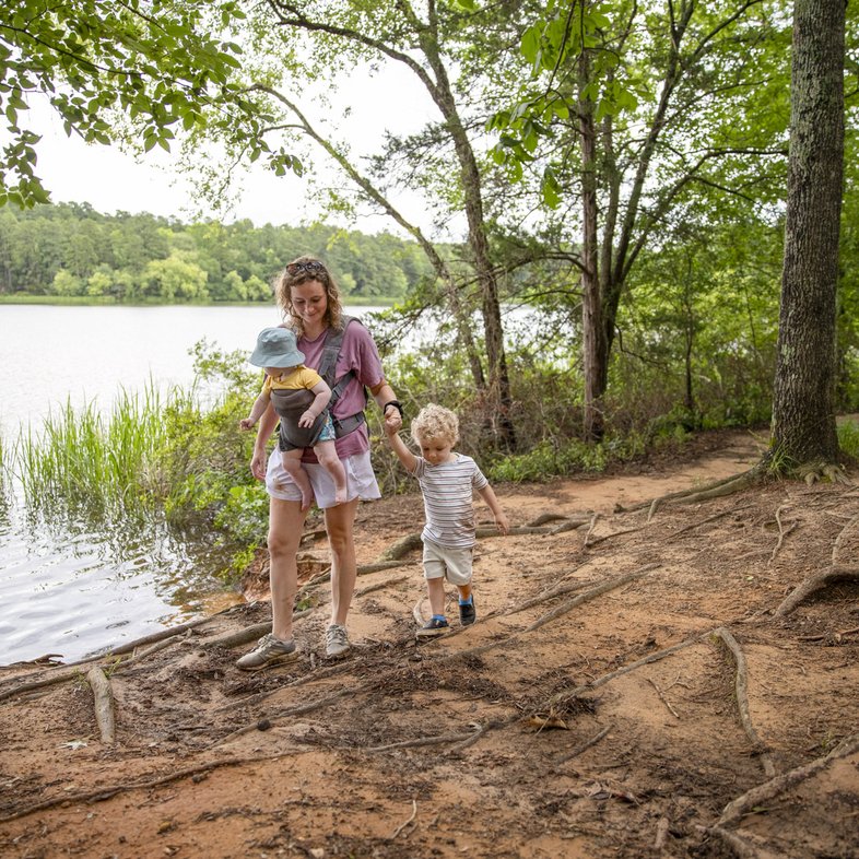 Mother and two kids hiking on dirt trail with tall trees next to lake in Tyler State Park